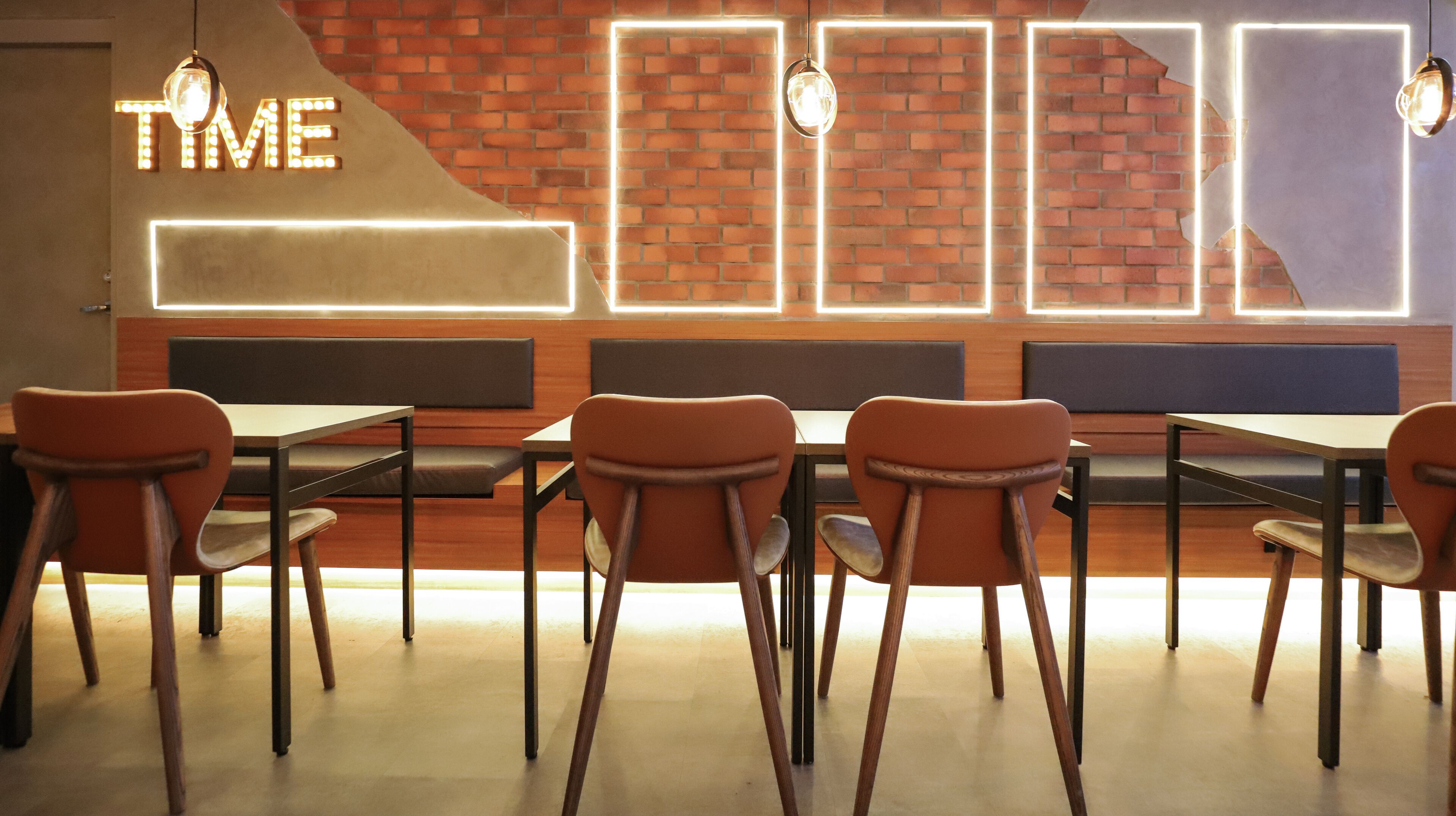 A restaurant interior with a brick wall, neon 'TIME' sign, wooden tables, and orange chairs.
