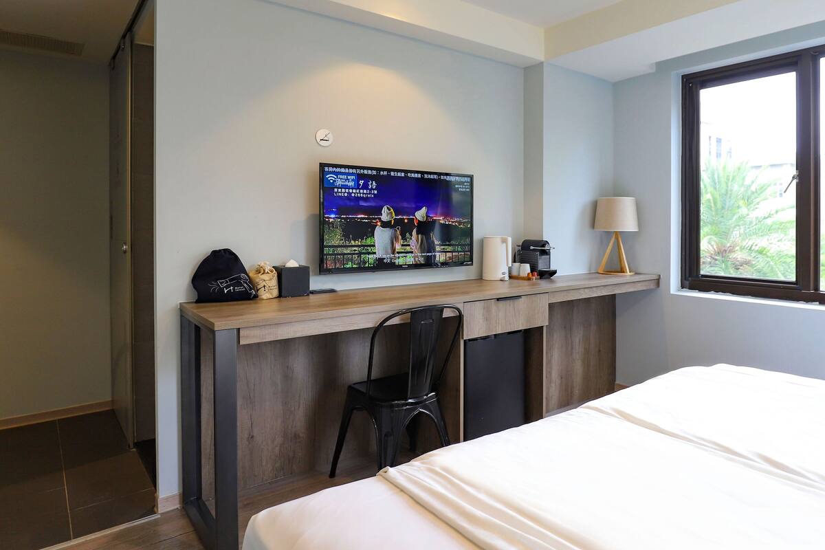 Een hotelkamer met een bed, een bureau met computer, een stoel, een televisie aan de muur en een raam met gordijnen.