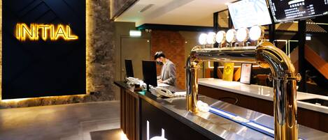 A reception desk with a modern design, a neon sign reading "INITIAL", and a digital screen displaying information.