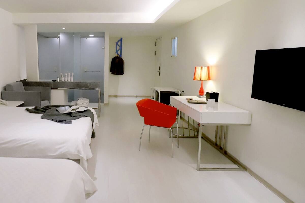 Een hotelkamer met twee bedden, een bureau met stoel, een televisie en een badkamer op de achtergrond.