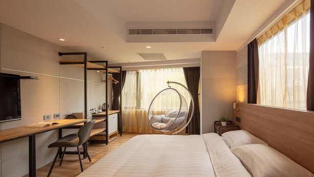 Una habitación de hotel moderna con una cama grande, un escritorio con una silla, un televisor y una silla colgante.