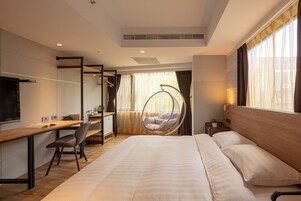 Een moderne hotelkamer met een groot bed, een bureau met stoel, een televisie en een hangstoel.
