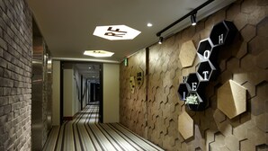 Pasillo de hotel con piso a rayas, paneles hexagonales en la pared y un letrero con el nombre del hotel.
