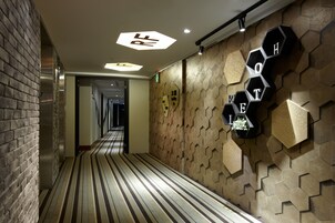 Een hotelgang met een gestreept vloerkleed, hexagonale wandpanelen en een bord met de naam van het hotel.