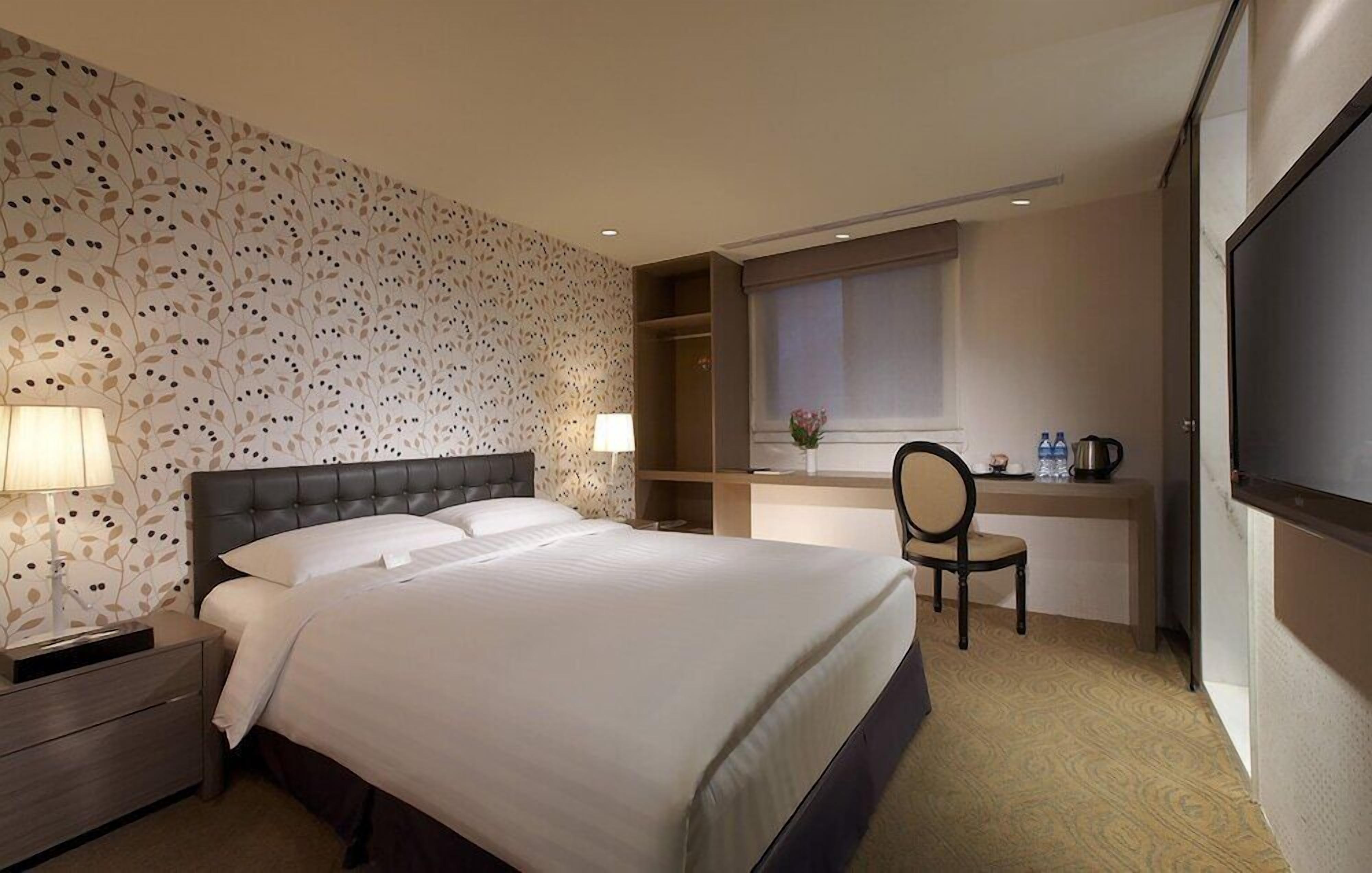 Een hotelkamer met een groot bed, bedlampen, een bureau met stoel en een televisie.