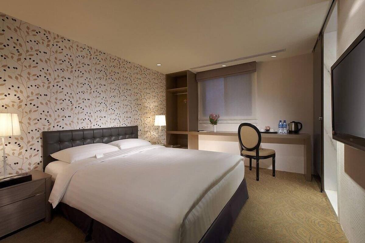 A hotel room with a large bed, bedside lamps, a desk with a chair, and a TV.