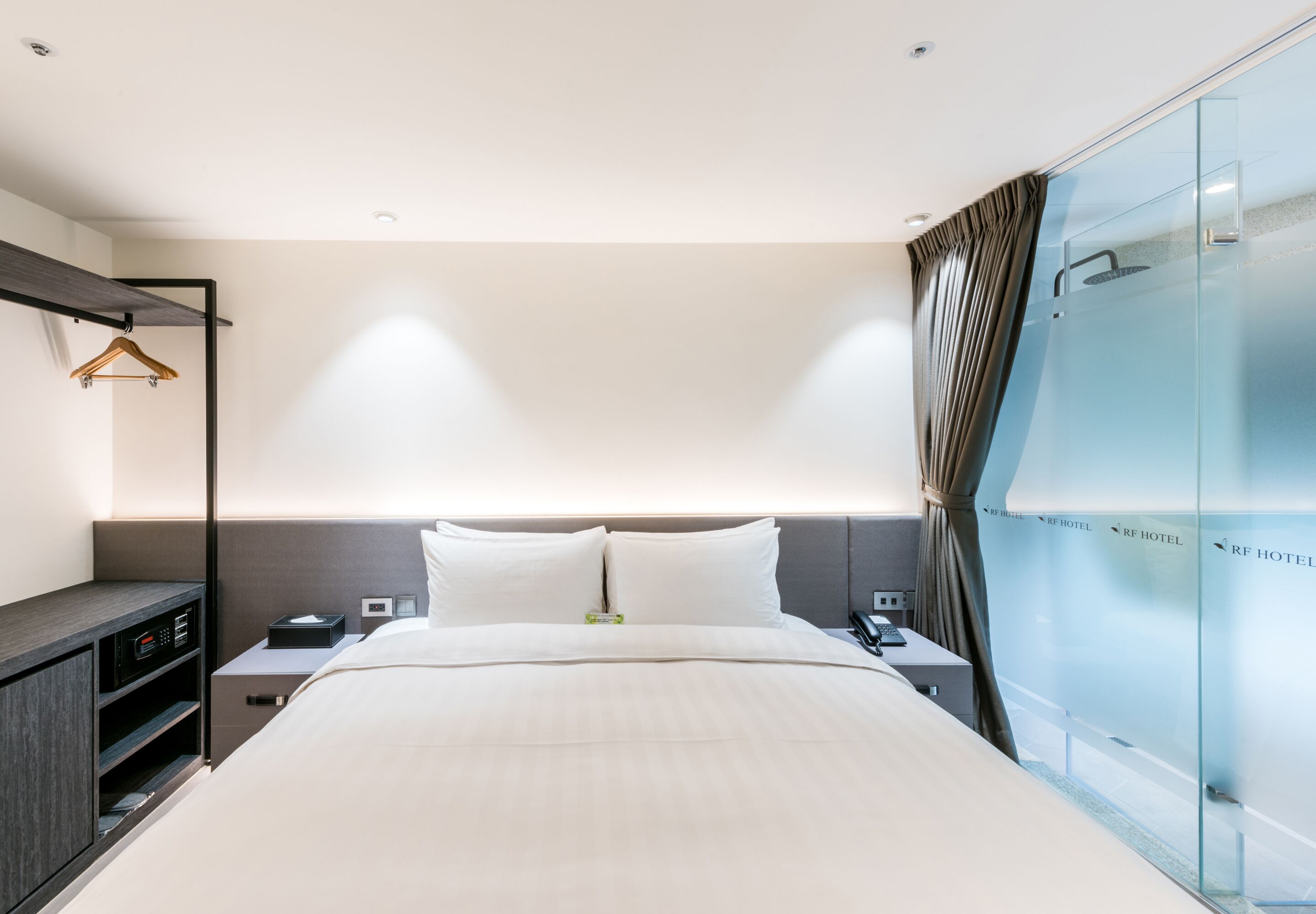 Ein modernes Hotelzimmer mit einem großen Bett, Nachttischen, einem Kleiderschrank und einer Glaskabine.