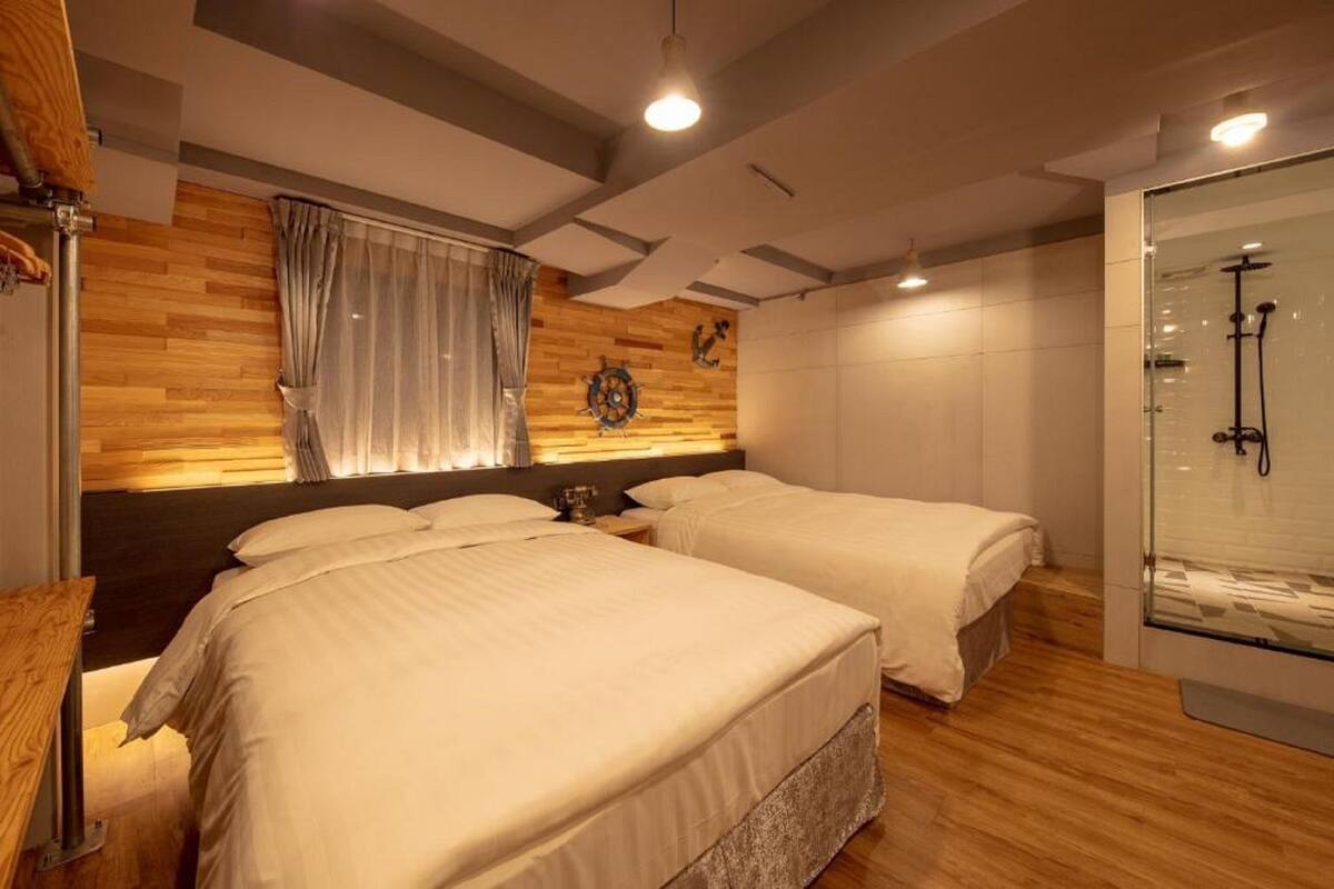 A hotel room with two beds, a wooden accent wall, a large mirror, and a glass shower enclosure.