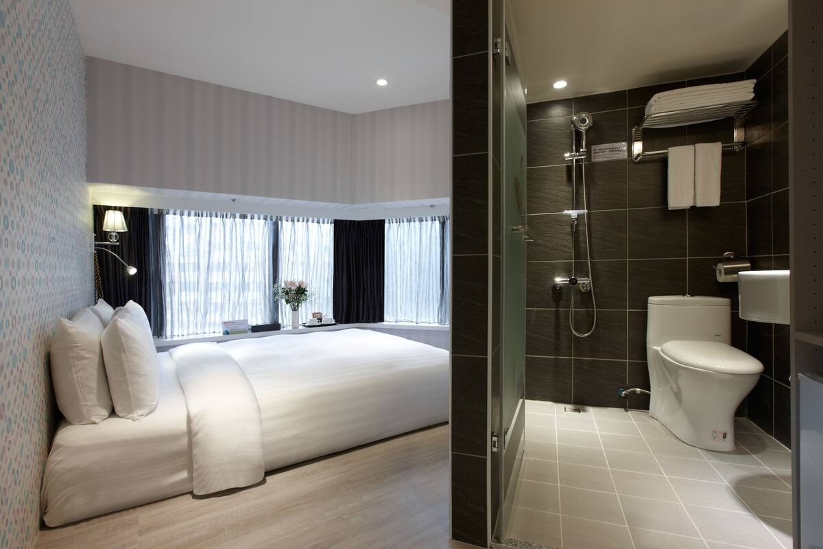 A modern hotel room with a large bed, a shower area, and a toilet.
