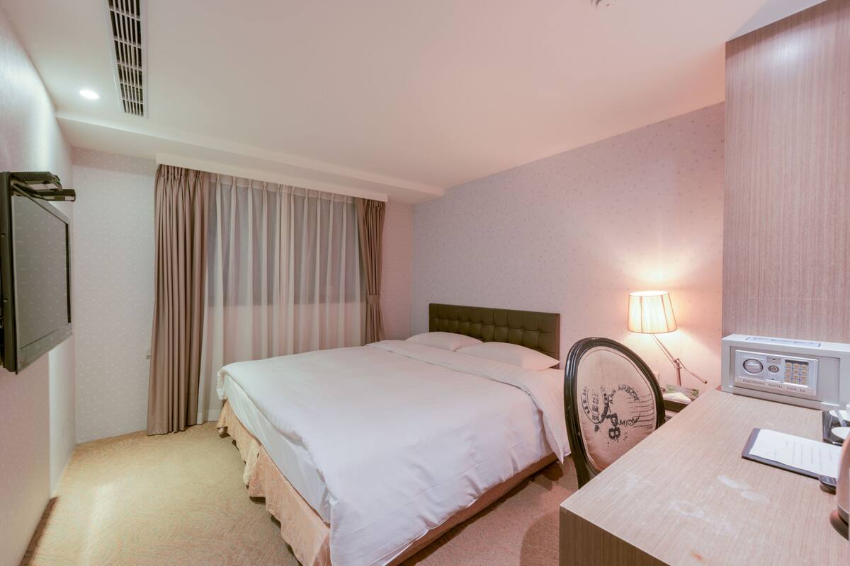 A hotel room with a bed, a desk, a lamp, and a radio.