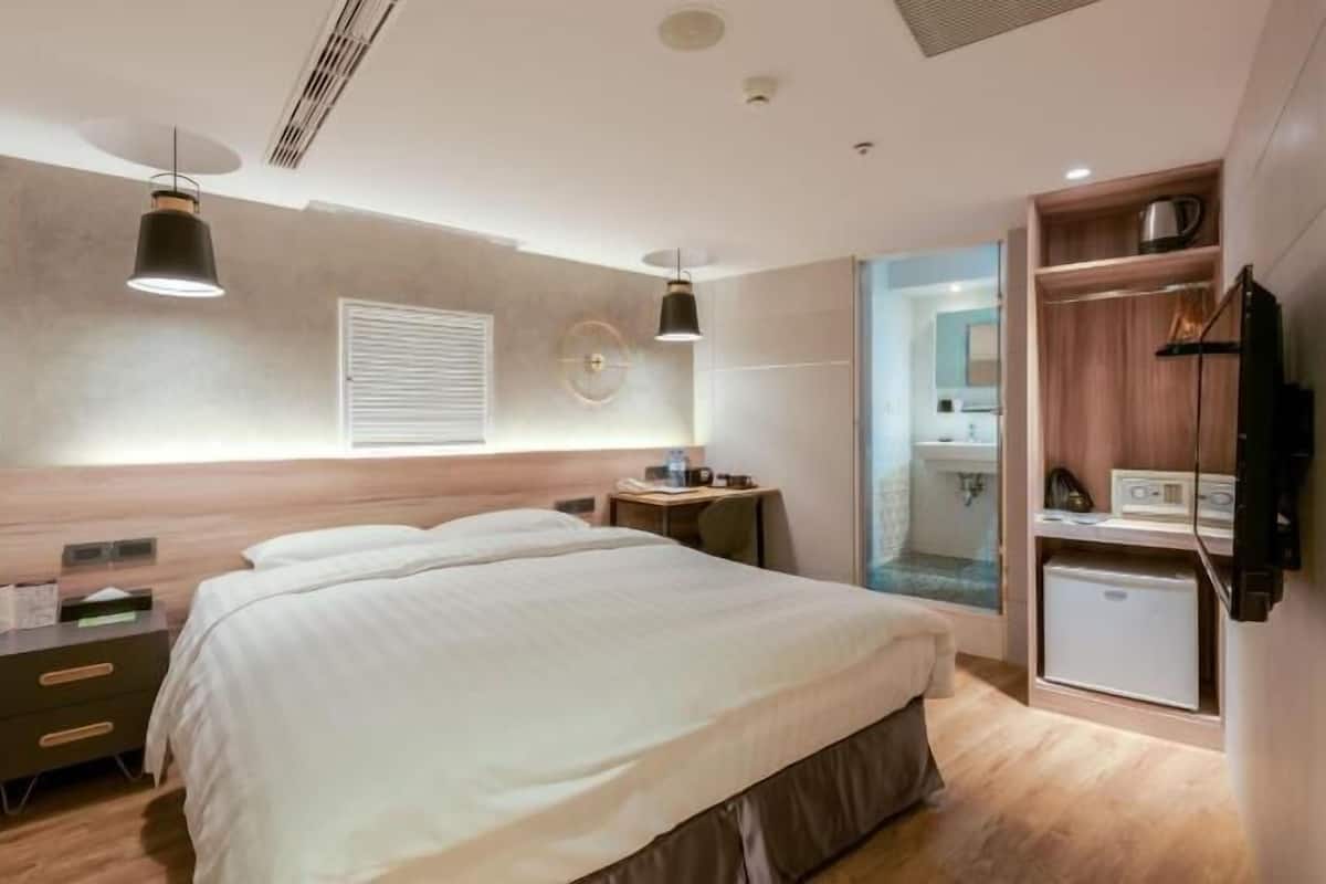 A modern hotel room with a bed, bedside tables, a TV, and a small kitchenette.
