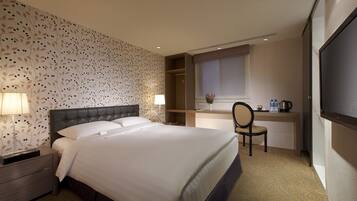 A hotel room with a large bed, bedside lamps, a desk with a chair, a window, and a TV.