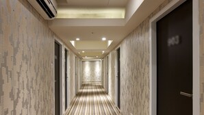 Un pasillo de hotel con papel tapiz estampado, alfombra a rayas y una puerta oscura a la derecha.
