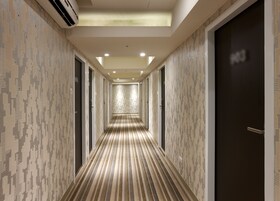 Een hotelgang met behang met patroon, een gestreept tapijt en een donkere deur aan de rechterkant.
