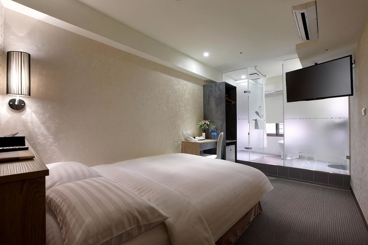 A hotel room with a bed, bedside table, lamp, and a TV.