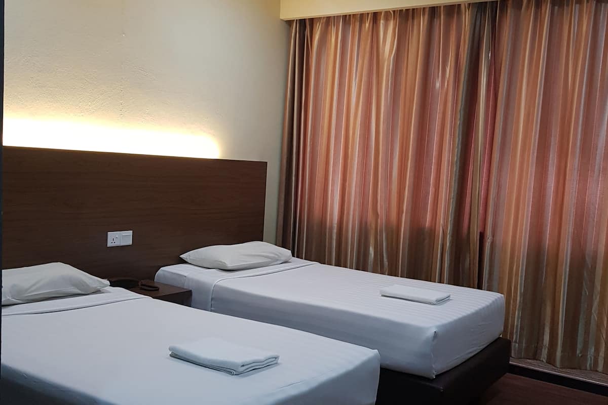 A hotel room with two beds, wooden headboards, a window with curtains, and a wall-mounted light.