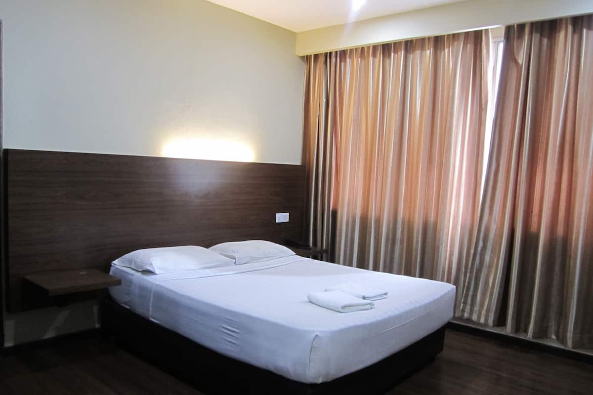 A hotel room with a bed, a nightstand, and a window with curtains.