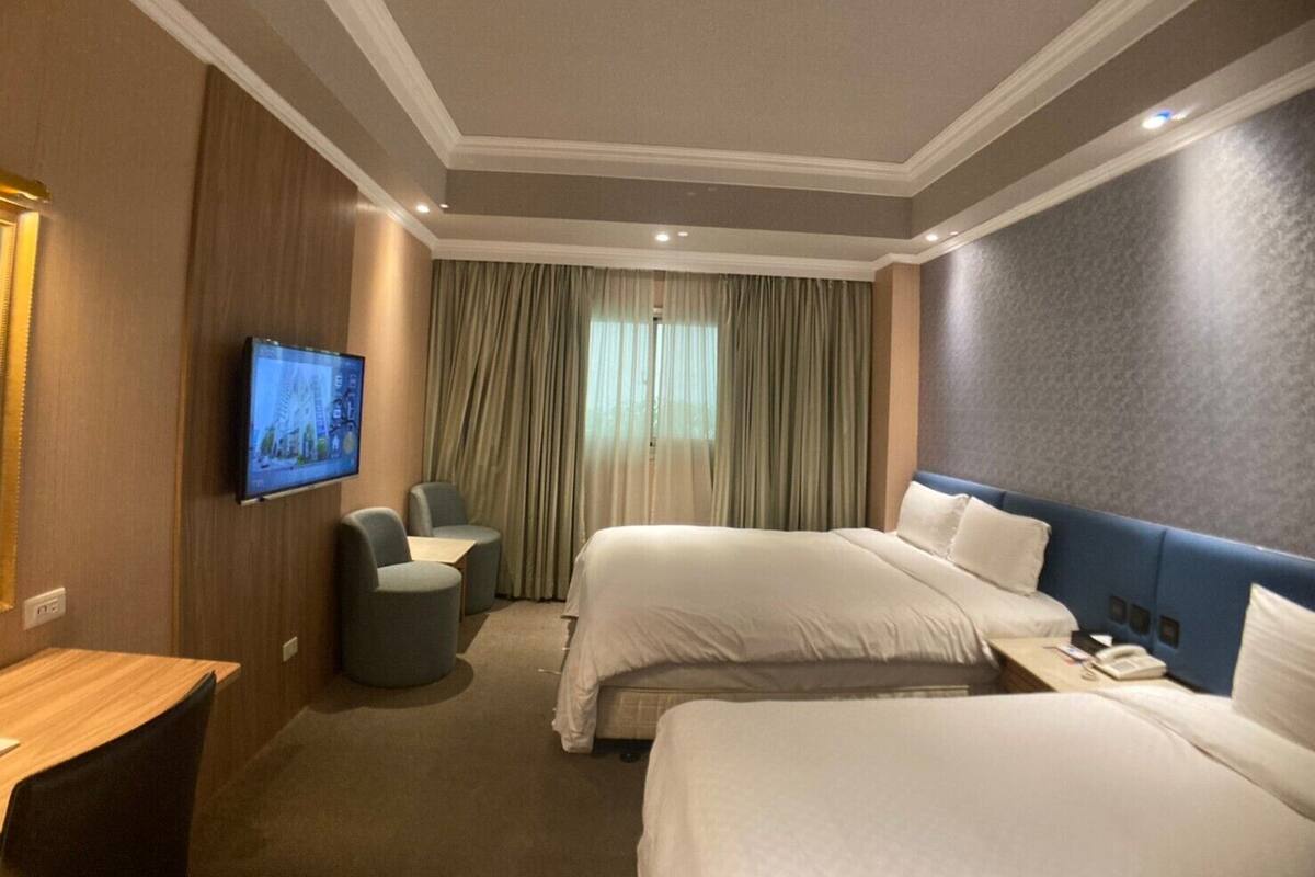 A hotel room with two beds, a desk, a chair, a television, and a window with curtains.