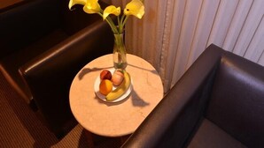 A small round table with a vase of yellow flowers, a plate of fruit, and a glass of water. - All Fun Business Hotel (Taichung)