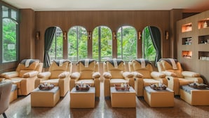 A spa room with multiple massage chairs, a reception desk, and a view of greenery through large windows. - Elite Suites Patong (Patong)