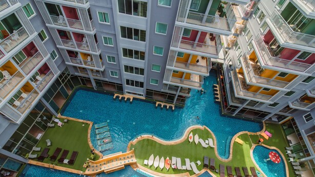 A multi-story hotel with a central swimming pool, balconies with railings, and outdoor seating areas. - Elite Suites Patong (Patong)