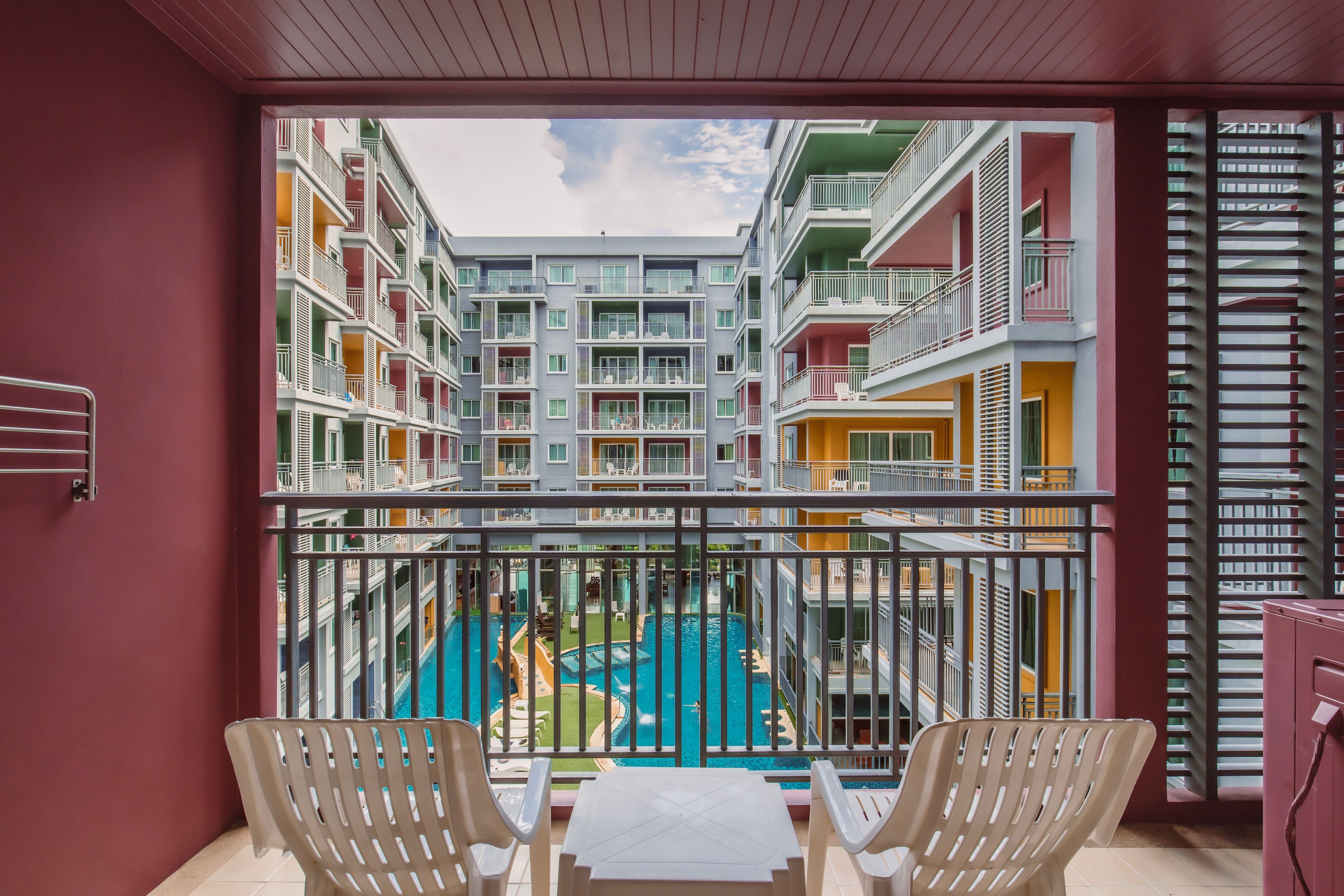 A balcony with a view of a swimming pool and multi-story buildings.