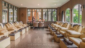A spacious lounge area with multiple sofas and a central table, large windows with arched frames, and a view of greenery outside. - Elite Suites Patong (Patong)