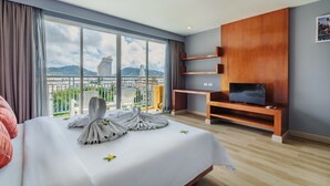 A hotel room with a large bed, a TV on a wooden stand, and a balcony with a city view. - Elite Suites Patong (Patong)