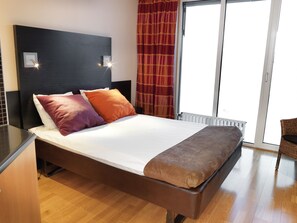 A modern bedroom with a large bed, two bedside lamps, a window with curtains, and a wooden floor.