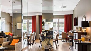 Un vestíbulo de hotel moderno con comedor, arreglos de asientos y una cocina visible a través del separador de vidrio.