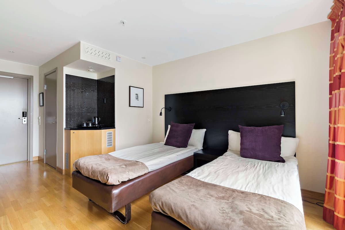 A hotel room with two beds, a kitchenette, and a bathroom.