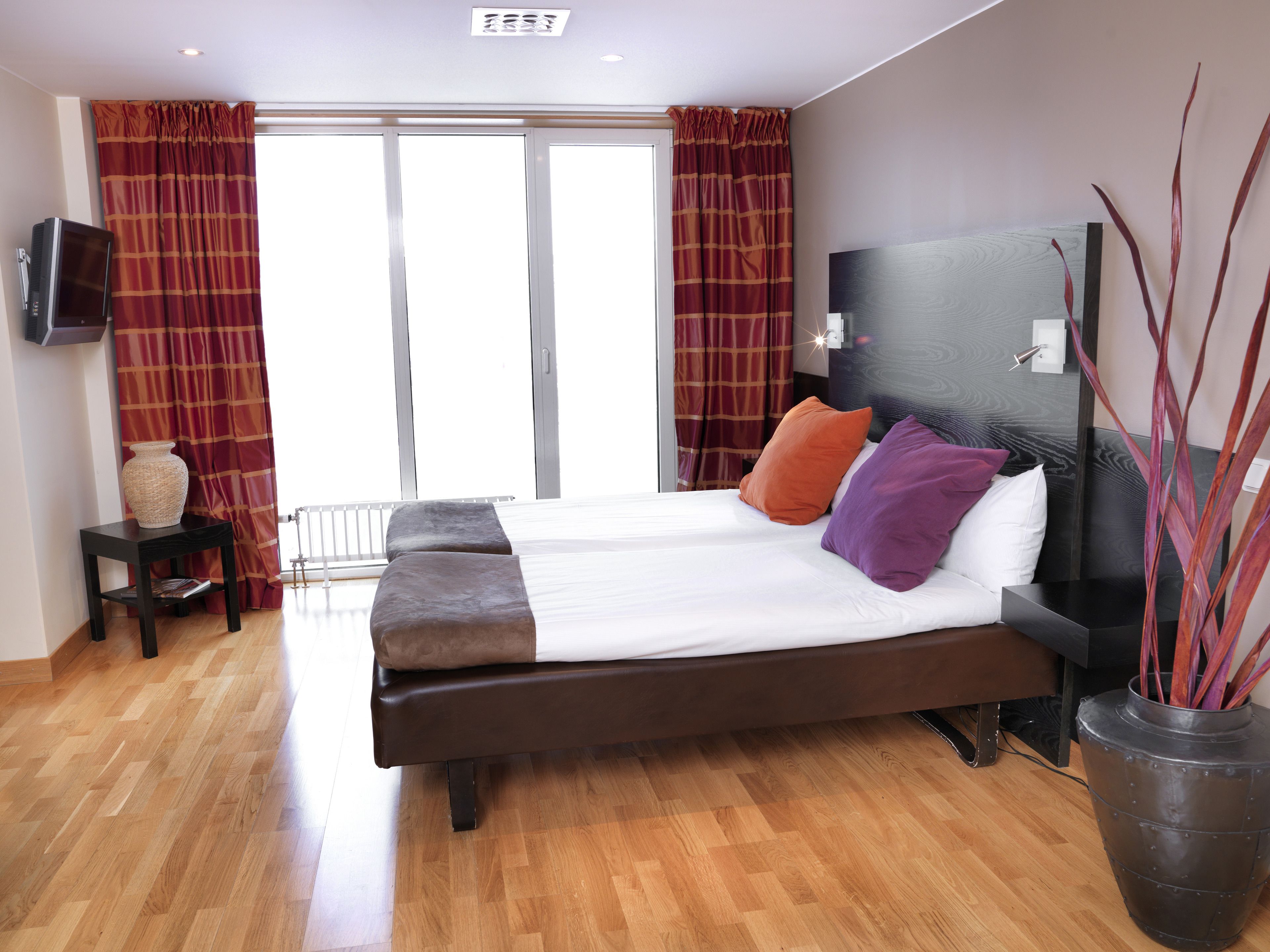 A modern hotel room with a large bed, a flat-screen TV, a small side table, and a potted plant.