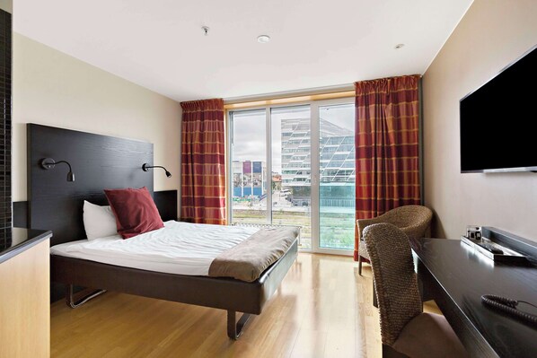Une chambre d’hôtel avec un lit, un bureau, une chaise, une télévision et une grande fenêtre avec des rideaux.