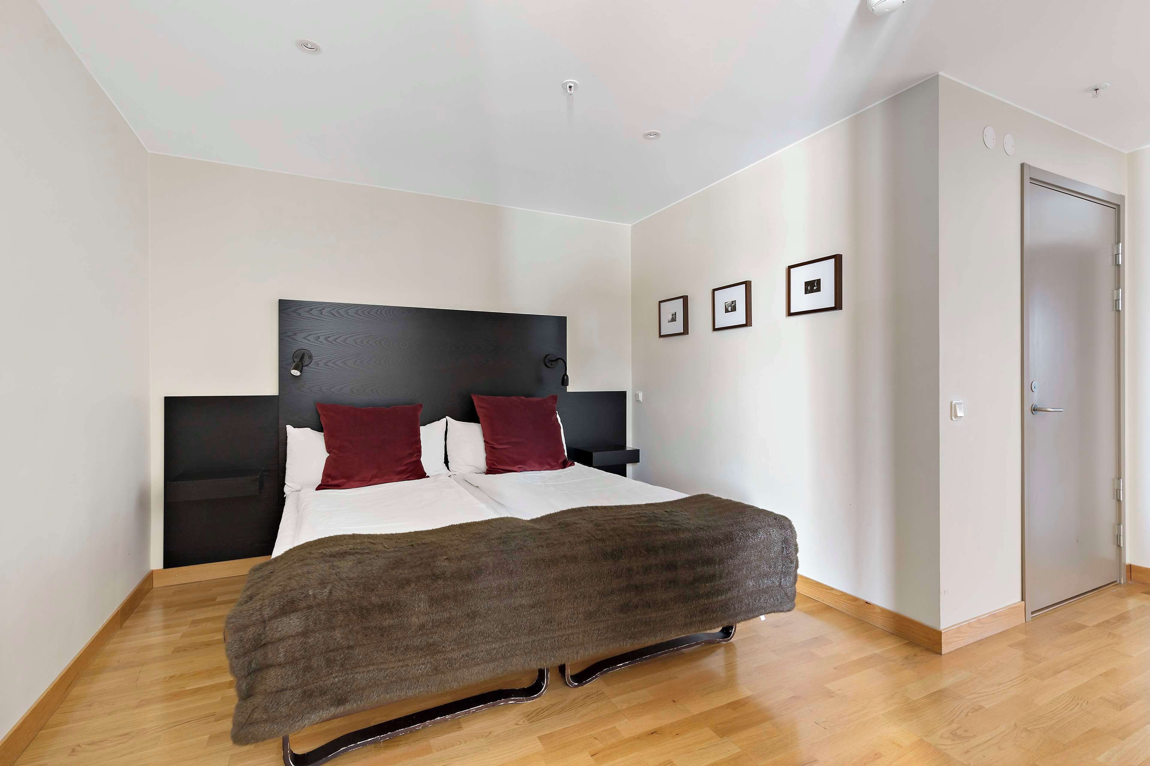A modern hotel room with a large bed, a dark headboard, and a wooden floor.