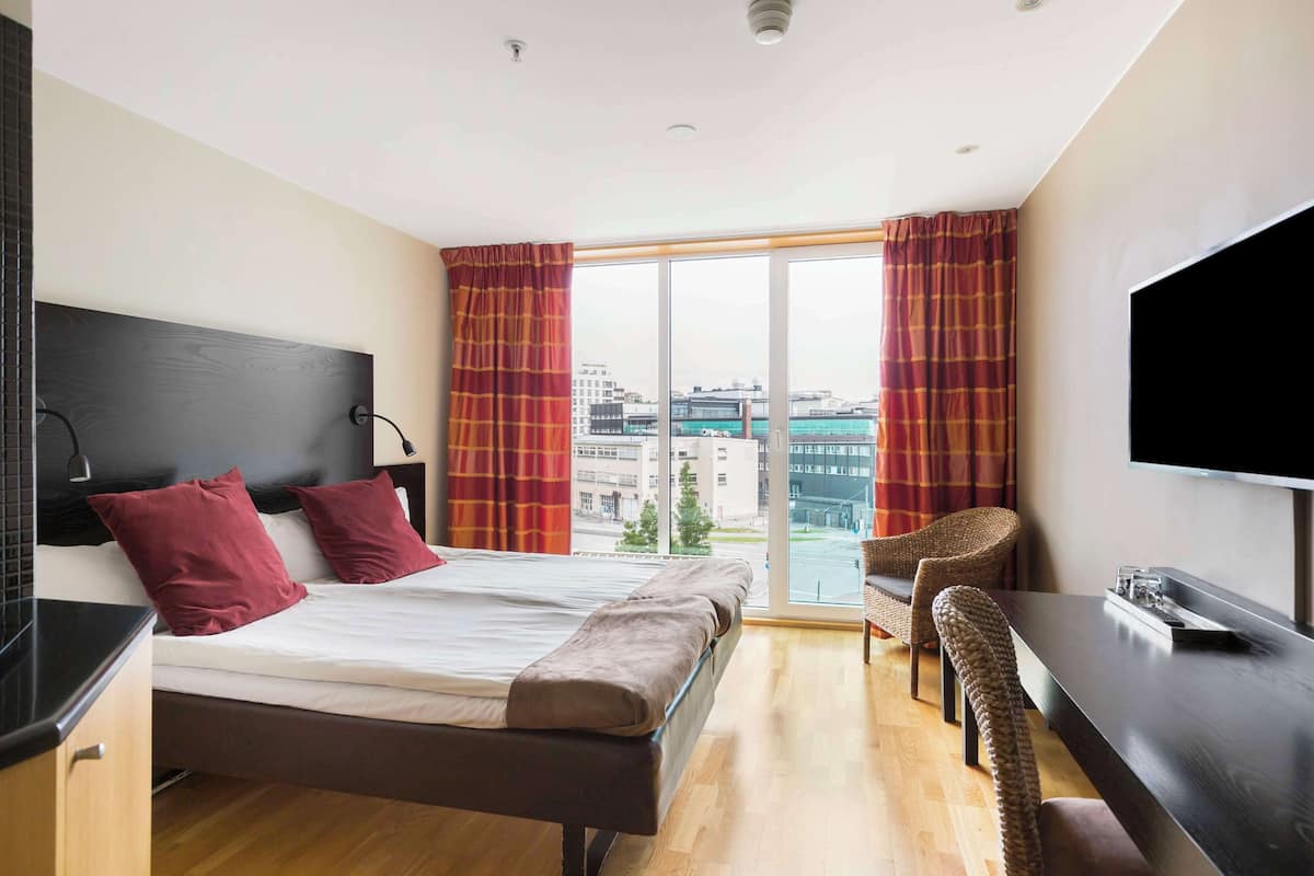 A modern hotel room with a large bed, a desk, and a TV.