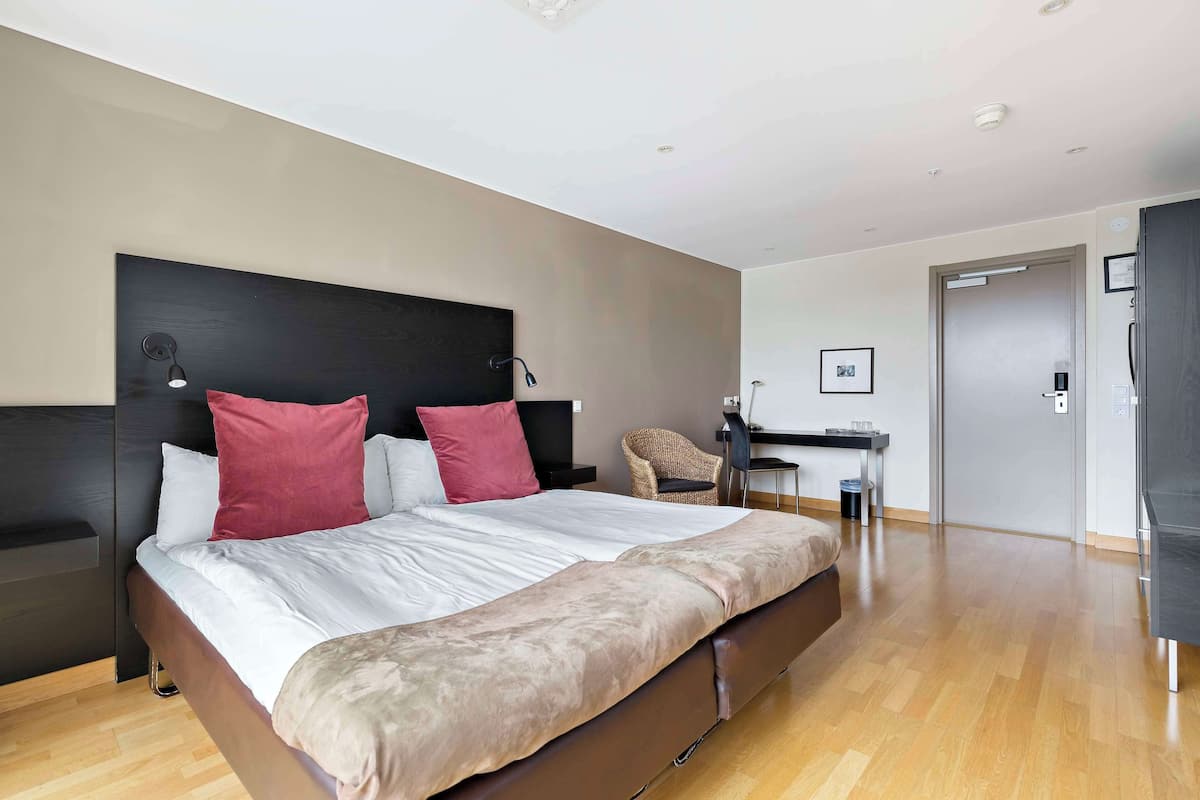 A modern hotel room with a large bed, a desk, and a chair.