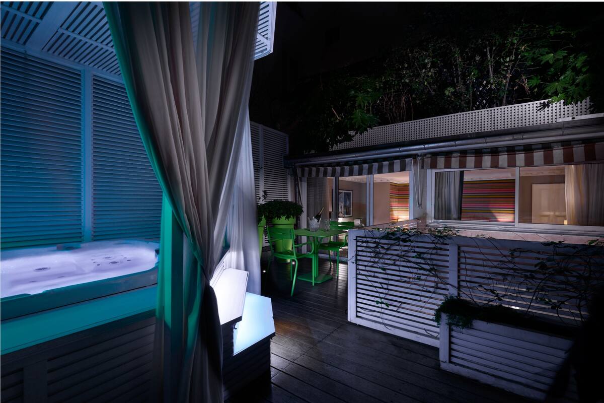 A covered outdoor area with a wooden deck, green chairs, a table, and a bench.