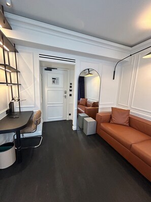A modern living room with a dark floor, a brown leather sofa, a round table with a chair, and a staircase with built-in lighting. - Hôtel Le Mathurin (Paris)