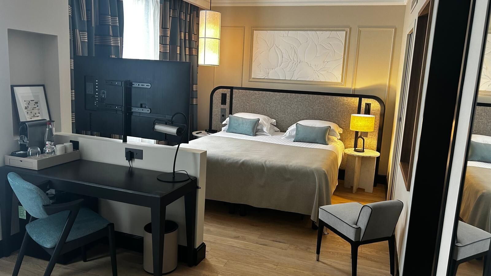 Een hotelkamer met een bed, nachtkastjes, een bureau met een stoel, een televisie en een lamp.