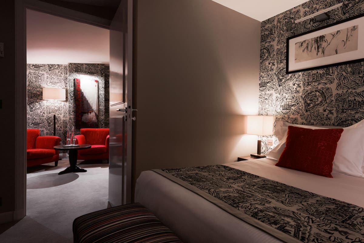 A hotel room with a bed, a red sofa, a small table, and a wall with a patterned wallpaper.