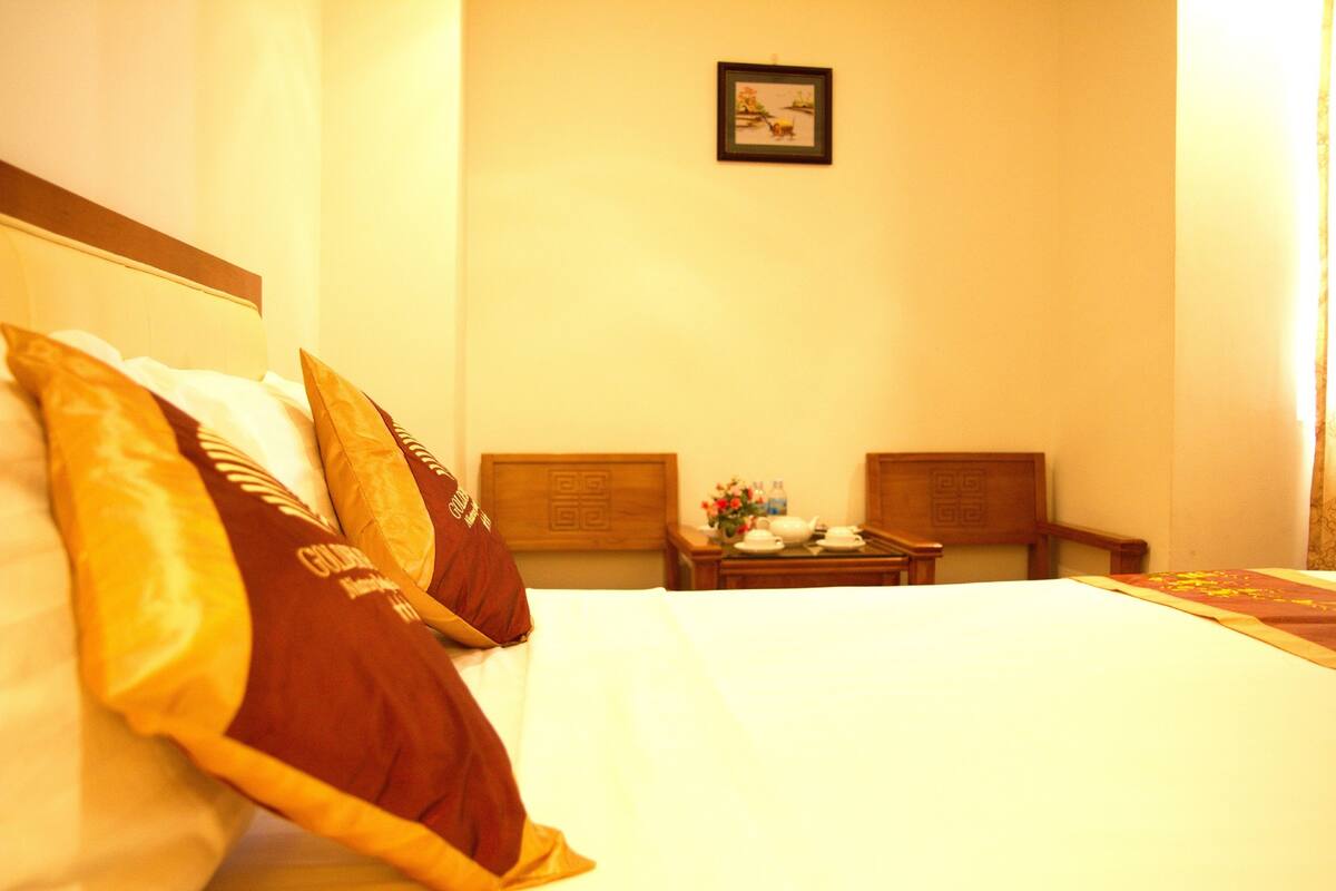 A hotel room with a neatly made bed, a small table with a vase of flowers, and two chairs.