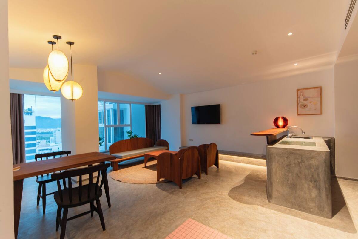 A modern living room with a sofa, a dining table with chairs, a TV mounted on the wall, and a unique lighting fixture.