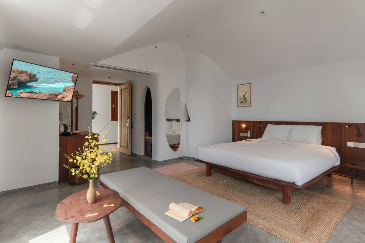 A modern hotel room with a bed, a TV, a desk, and a seating area.