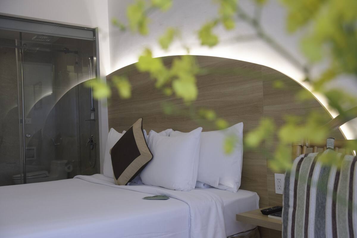 A hotel room with a bed, a nightstand, a shower area, and a view of the outdoors.