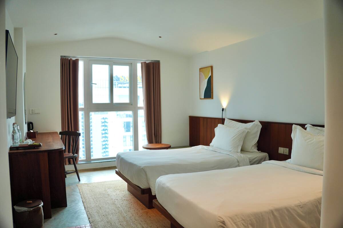 A hotel room with two beds, a desk, and a view of the outside.