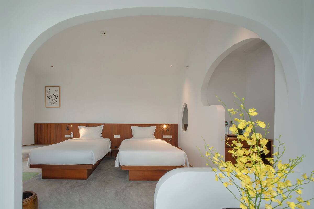 A modern hotel room with two beds, a wooden headboard, a small table, and a vase of yellow flowers.