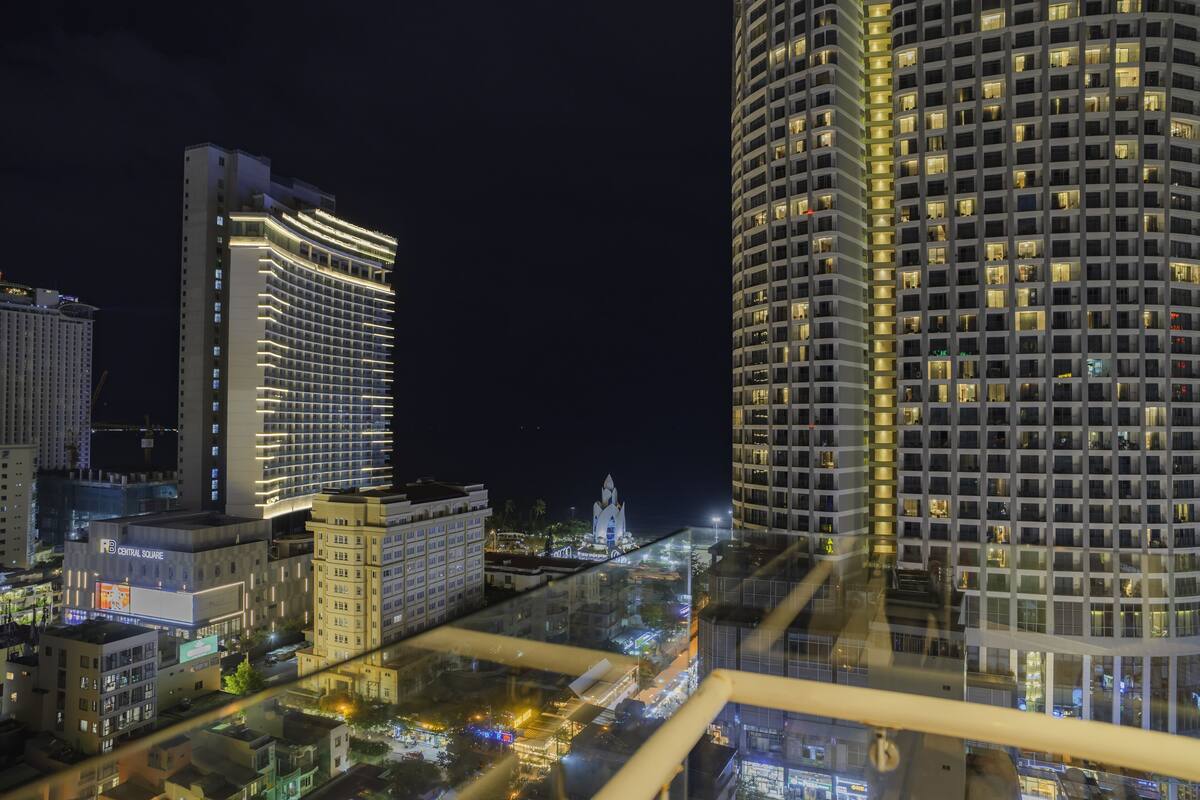 A nighttime cityscape with illuminated high-rise buildings, a prominent hotel with a lit facade, and a distant tower structure.