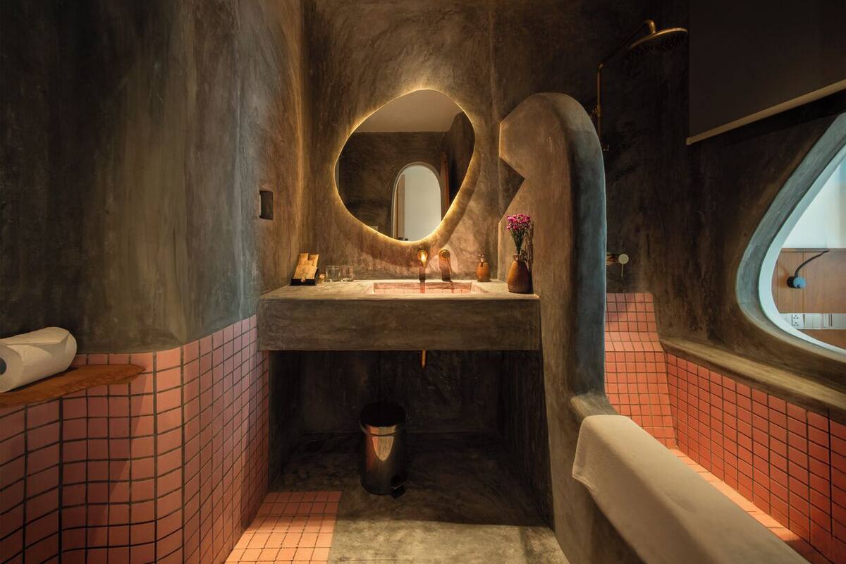 A bathroom with a curved sink, a round mirror, and a window.