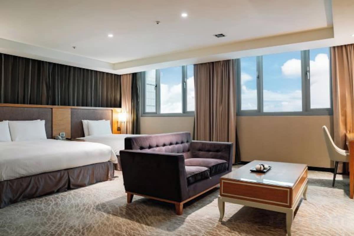 A hotel room with a large bed, a sofa, a coffee table, and a chair.