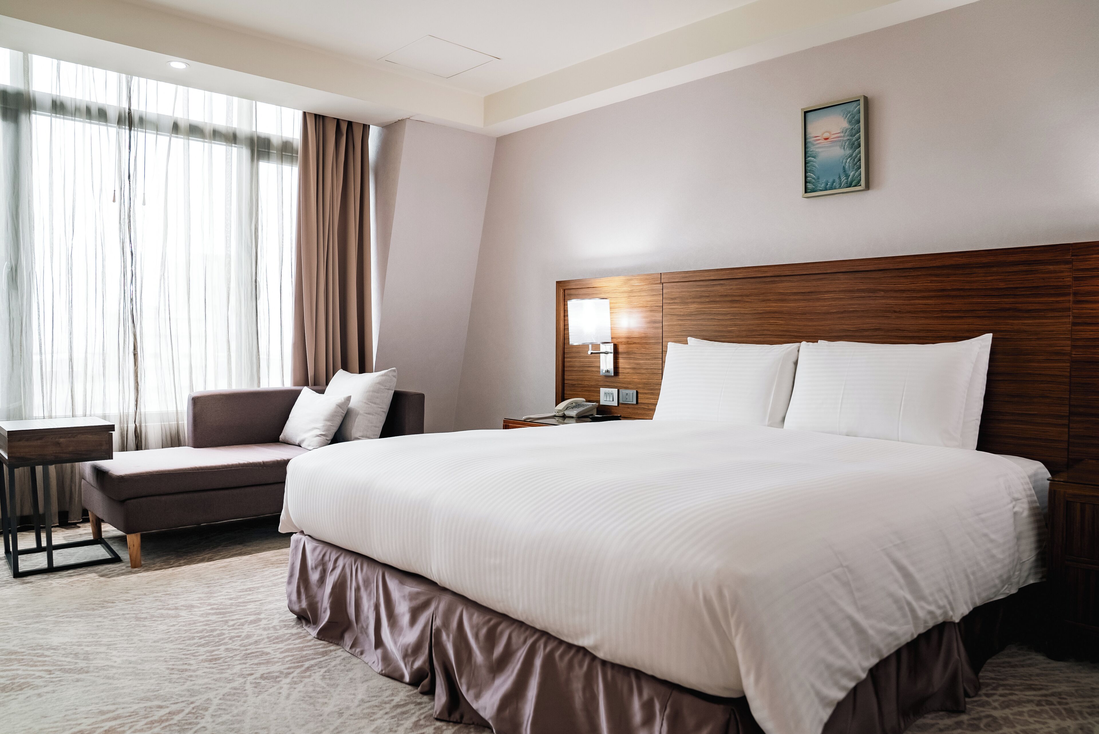 Una habitación de hotel con una cama grande, un escritorio, una silla y un ventanal con cortinas.